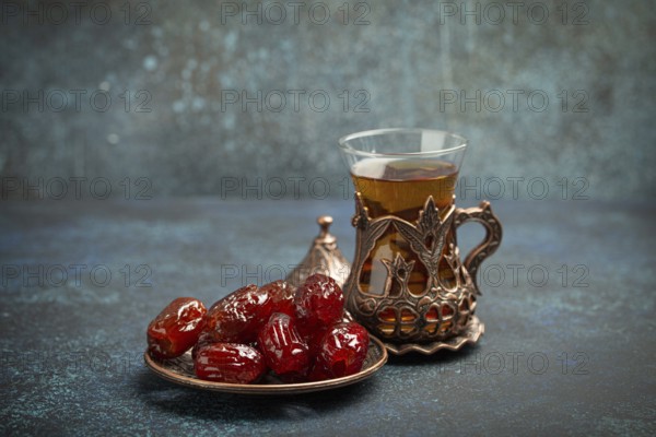 Breaking fasting with dried dates during Ramadan Kareem, Iftar meal with dates and Arab tea in traditional glass, angle view on rustic blue background. Muslim feast, food photography, food photography