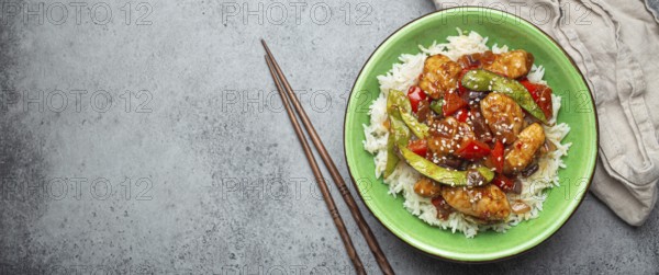 Asian sweet and sour sticky chicken with vegetables stir-fry and rice in ceramic bowl with chopsticks top view on gray rustic stone background, traditional Asian dish. Space for text, food photography, food photography