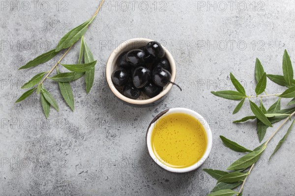 Black olives and extra virgin olive oil in little bowl with olive tree branches top view on gray concrete stone background, food photography, food photography