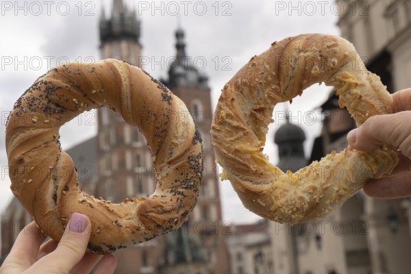 Tourist woman eating bagel obwarzanek traditional polish cuisine snack waling on Market square St. Mary's Basilica on the Krakow Main Square Rynek Glowny Poland. Krakow architecture, old city architecture. Historic Roman Catholic church in Krakow Baroque architecture Travel tourist attraction