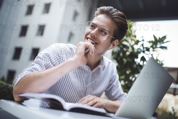 Happy handsome businessman mixes his break and job outdoors, businessman with headphones write some new ideas in notebook sitting in cafe