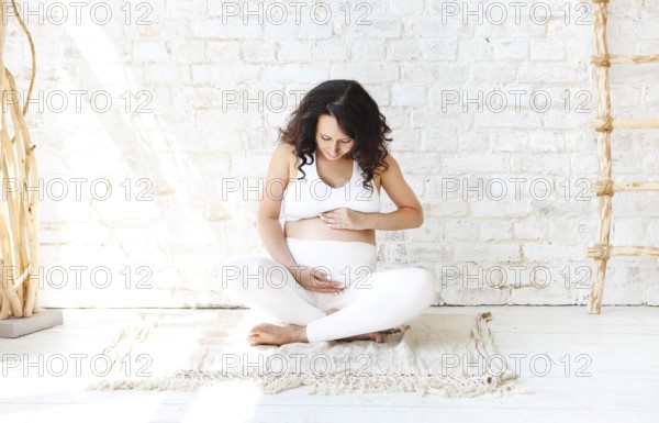 Beautiful brunette pregnant woman stretching and practicing yoga at home