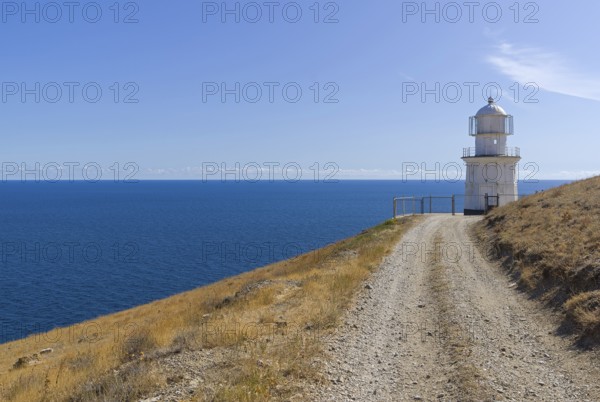 A dirt road running along a deserted mountainside to a lighthouse on the seashore. Cape Meganom, Crimea, a sunny day in September