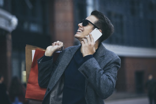 Positive cool guy with sunglasses and paper bags walking near showcase with reflection