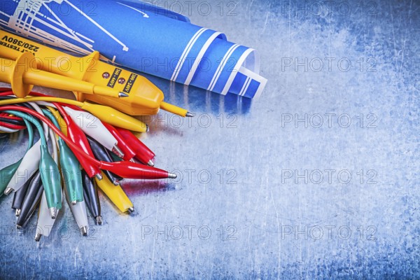 Yellow electrical tester crocodile cables set blue construction plans on metallic background electricity concept