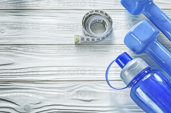 Dumbbells measuring tape water bottle on wooden board fitness concept