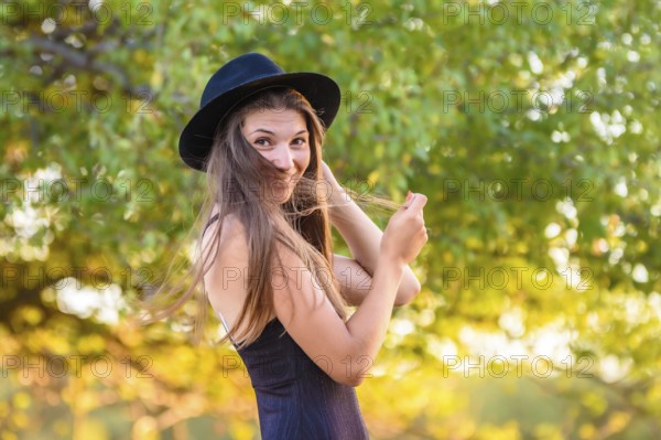 Portrait of a beautiful girl against a background of blurry foliage, the girl temptingly covered her face with a lock of hair