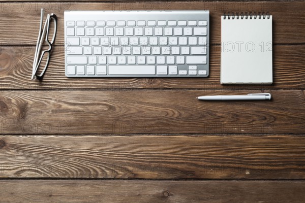 Still life of office workspace with supplies. Flat lay old wooden desk with white computer keyboard, pen and notebook. Top view business concept. Vintage brown wooden surface with copy space