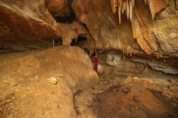 A speleologist with helmet and headlamp exploring a cave with rich stalactite and stalagmite formations. graphy