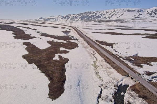 Aerial view of plateau landscape with snow covering the ground and Austertanaveien road 890 in sunny summer weather, Varanger Peninsula, Norway, Europe