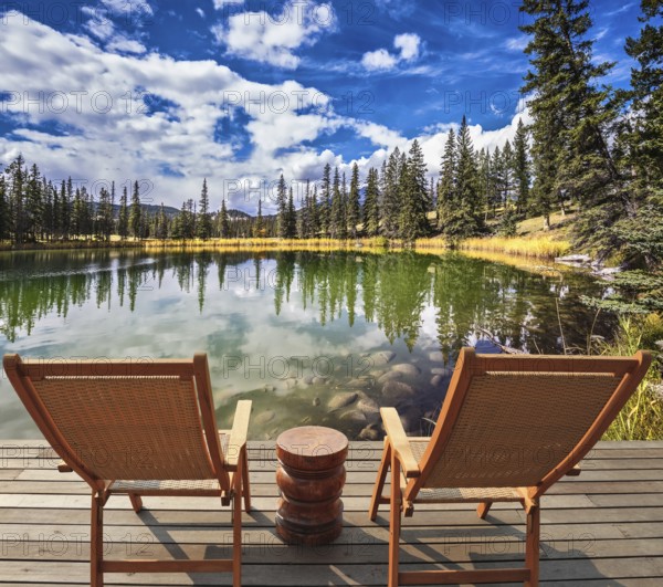 Adorable lake. Two wooden deckchairs for tourists. Coniferous forest is reflected in the mirrored water of lake. Warm autumn day in Jasper National Park in the Rocky Mountains