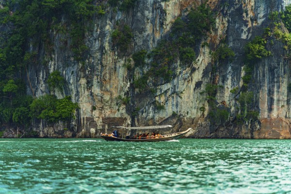 Longboat navigating along a towering cliff with greenery above turquoise water, Cheow Lan Lake, Khao Sok National Park, Thailand, National Park, Khao Sok lake, water, mountains, green, Asia