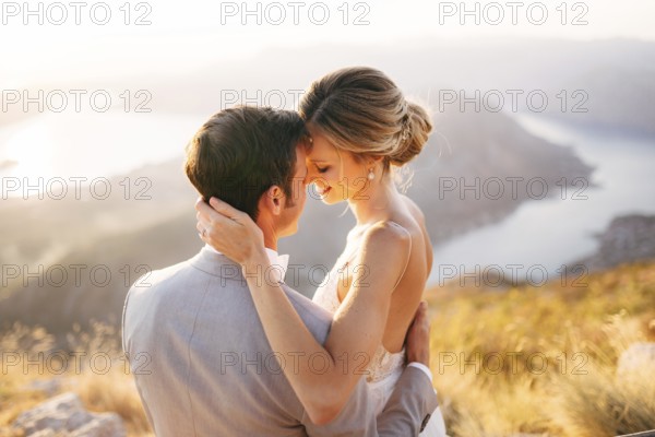 The bride and groom sitting on the top of Mount Lovcen overlooking the Bay of Kotor, smiling and hugging tenderly, close-up .