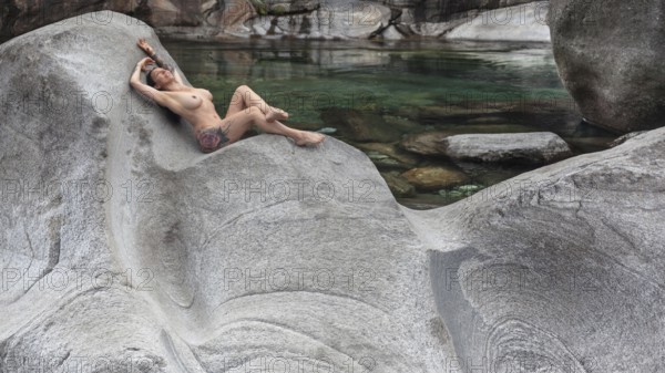 A woman lying in a comfortable position on a smooth granite rock on the bank of a river, Verzasca Valley, Valle Verzasca, Canton Ticino, Switzerland, Europe