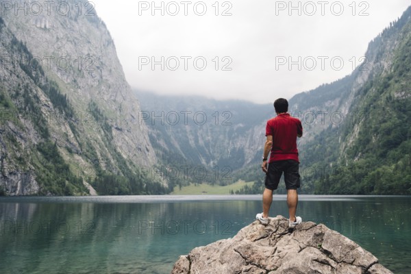 Man standing on rock looking at beautiful and misty lake in the alps. Obersee