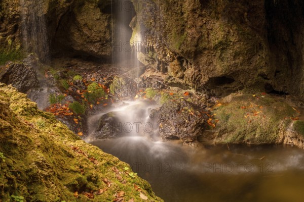 Closeup view of a forest waterfall in sunlight with autumn leaves and mossy stones