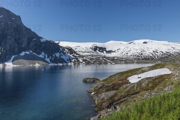 The famous road in Norway also called road 51 or the bygdin vegen near Bismo with blue water in the fjord and white snoiw on the mountains in summer