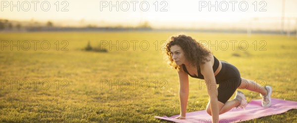 A woman holds a plank position on a mat in a field at sunset