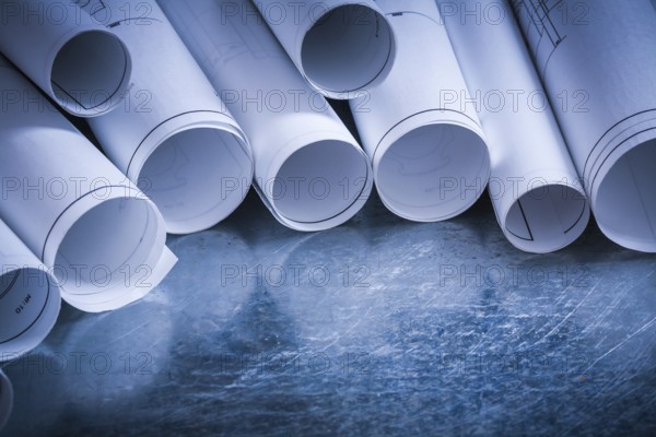 Set of rolled up white construction drawings on scratched silver-metal surface building and architecture concept