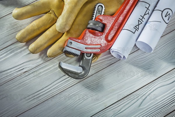 New plumb wrench leather gloves and rolled piping blueprints on vintage wood background