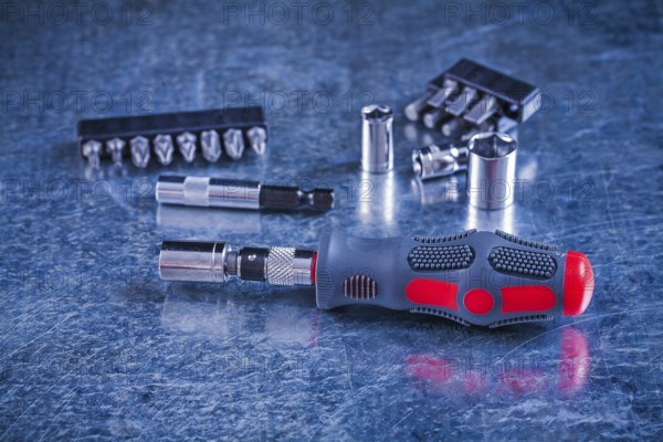 Insulated screwdriver with interchangeable bits and heads on scratched metallic background construction concept
