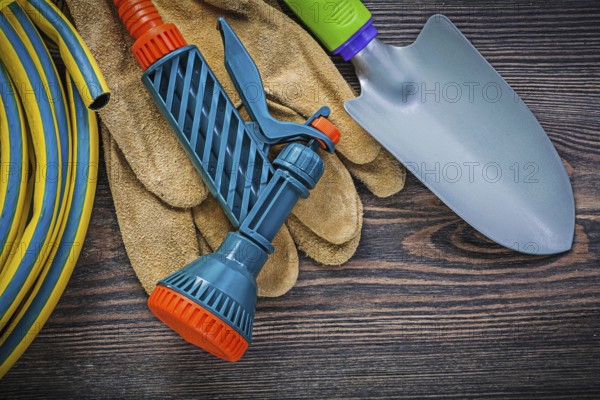 Coiled garden rubber hose protective gloves hand shovel on wood board gardening concept