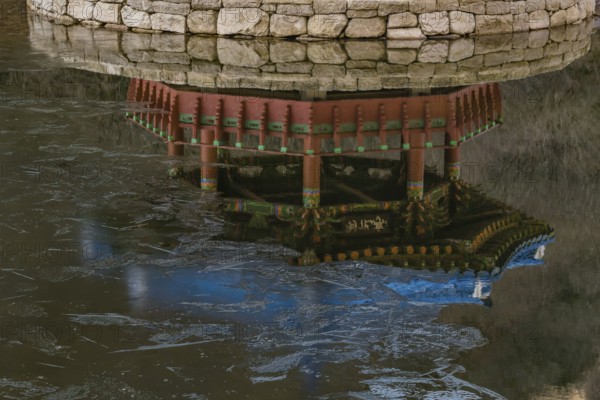 Jeongeup-si, South Korea. December 8, 2020: Reflection in water of picnic pavilion with blue roof on stone island in middle of pond