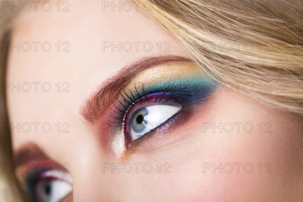 Close up portrait of a beautiful young blond model with bright make up. Close up of abstract multicolor make up. Makeup Pigment powder explosion