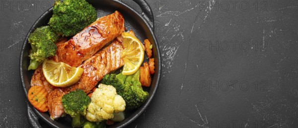 Healthy baked fish salmon steaks, broccoli, cauliflower, carrot in cast iron casserole bowl black dark stone background. Cooking a delicious low carb dinner, healthy nutrition, food photography