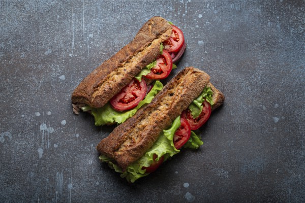Two dark ciabatta sandwiches with green salad, ripe red tomatoes, onion and tuna on rustic concrete stone background top view. Vegetable vegetarian sandwiches, healthy snack or lunch, food photography, food photography