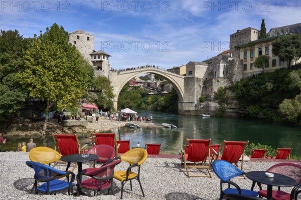 Cafe with colourful chairs on the banks of the river Neretva, behind the bridge Stari Most, old town of Mostar, Bosnia-Herzegovina