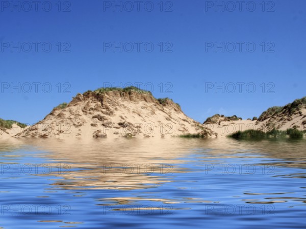 The beach from the sea at formby merseyside with tall sand dunes covered in rough grass and a blue summer sunlit sky