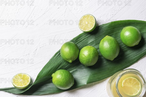 Bunch of limes on a big green leaf and a jar with freshly squeezed lime juice, on a white background. Above view with copy space. Detox context