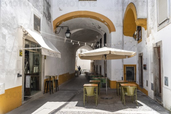 Evora, Portugal, June 30, 2022: Narrow street in the old town with restaurant terraces. Alentejo, Portugal, Europe