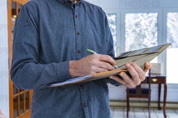 Inspector holding a notebook in his hand. Close-up of man's hands taking notes while standing indoor during home inspection, house interior background