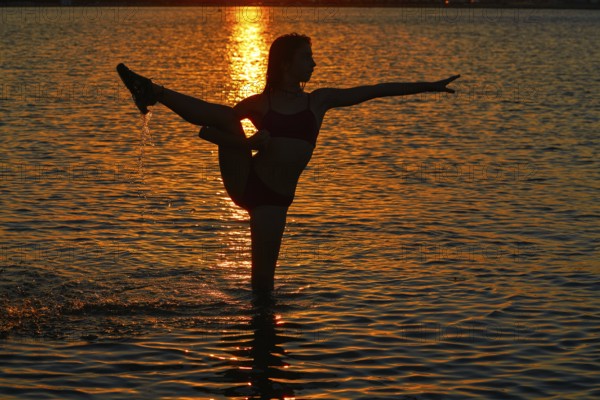 Girl gymnastics pose at sunset beach in orange sky