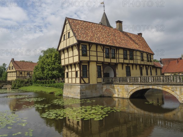 Half-timbered house stands picturesquely on a watercourse with water lilies and a stone bridge, steinfurt, münsterland, germany