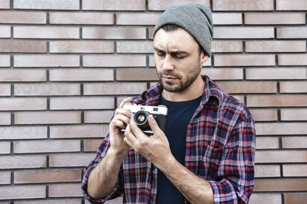 Man with retro photo camera Fashion Travel Lifestyle outdoor while standing against brick wall background