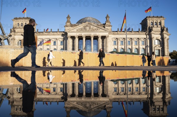 21.10.2023, Berlin, Germany, Europe, People walk past the Reichstag in Berlin's Mitte district on a sunny autumn day, its west façade reflected in a large puddle in front of it. On the façade of the Reichstag building above the portal is the lettering, Europe