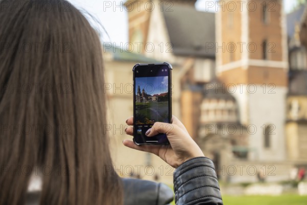 Female traveler in historical places looks around courtyard of landmark and shoots short video on phone. Tourist photographs historic place on sunny day. Unrecognizable woman Tourism and blogging sharing live online for audience travel together recording video on mobile phone