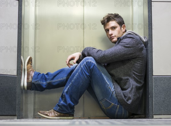 Handsome young man sitting in front of elevator (lift) doors, looking at camera