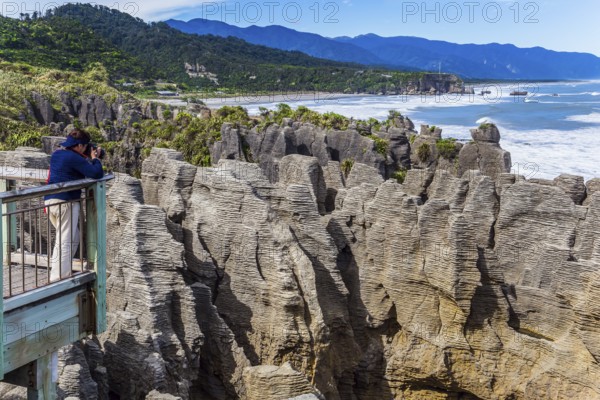 Observation deck. Woman takes pictures of rocks and ocean surf. New Zealand. Stone flat pancakes, stacked on top of each other. The concept of ecological, active and photo tourism