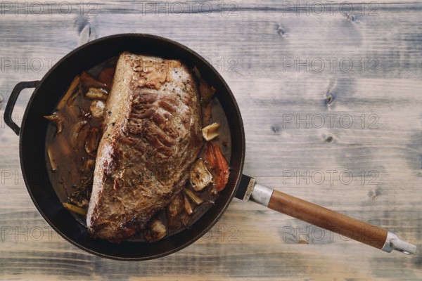 Juicy roast beef with a baked crust in vegetables and sauce stands in a pan on the table.