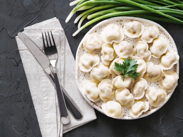 Traditional russian pelmeni, ravioli, dumplings with meat on black concrete background. Top view or flat lay. Russian food and russian kitchen concept