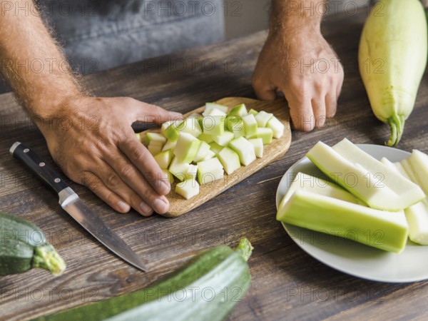 Zucchini harvest. Man slices zucchini cubes for freezing on wooden table. Farm organic zucchini harvesting