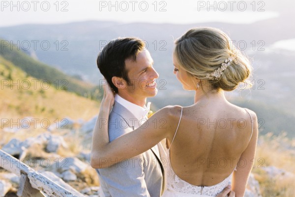 Bride sits on the lap of groom, hugging his shoulders.