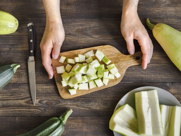 Zucchini harvest. Woman slices zucchini cubes for freezing on wooden table. Farm organic zucchini harvesting Top view or flat lay