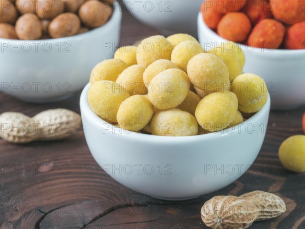 Peanut snack for beer, wine, party bar. Salted peanuts in yellow cheese glaze on brown wooden table. Copy space