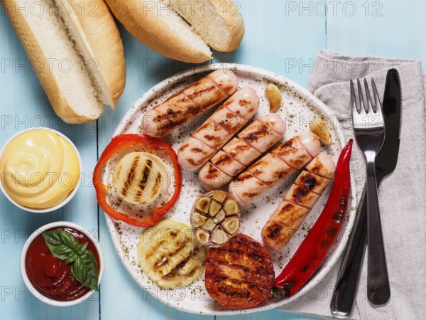Top view of chicken homemade sausages, buns bread, sauces ketchup and mustard on blue wooden background. Grilled sausages and grilled vegetables in craft trendy plate. Homemade hotdogs