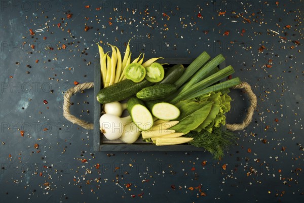 FRESH VEGETABLES ON WOODEN BOX ON A DARK STONE BACKGROUND. THE CONCEPT OF VINTAGE. THE YOUNG CORN ONIONS ASPARAGUS GREEN TOMATO CUCUMBER ON A DARK SURFACE